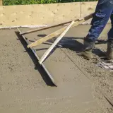Pracownik wylewa betonową wylewkę za pomocą łaty.
