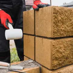Budowa płotu z bloczków betonowych: ręka w czerwonej rękawicy z młotkiem gumowym i kielnia.