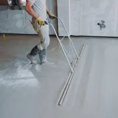 Robotnik wylewa beton na podłogę za pomocą zgarniacza.