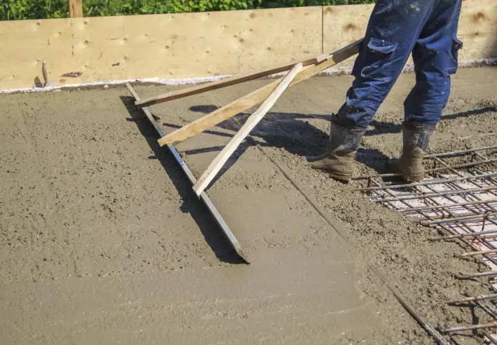 Pracownik wylewa betonową wylewkę za pomocą łaty.