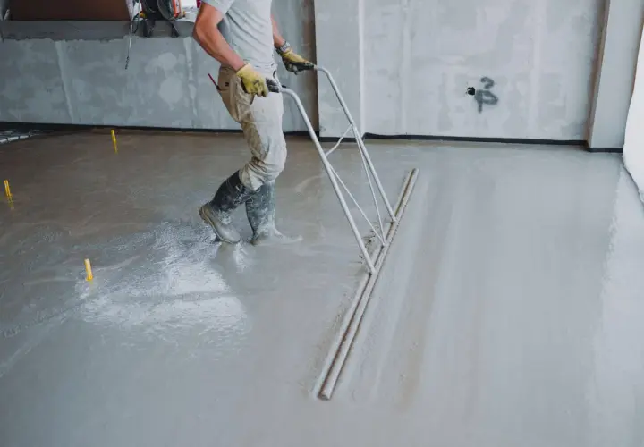 Robotnik wylewa beton na podłogę za pomocą zgarniacza.