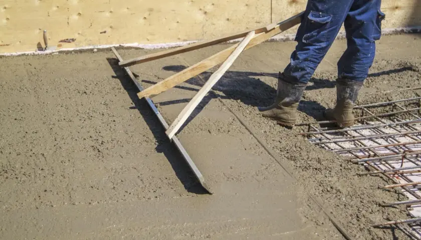 Pracownik wylewa betonową wylewkę za pomocą łaty.