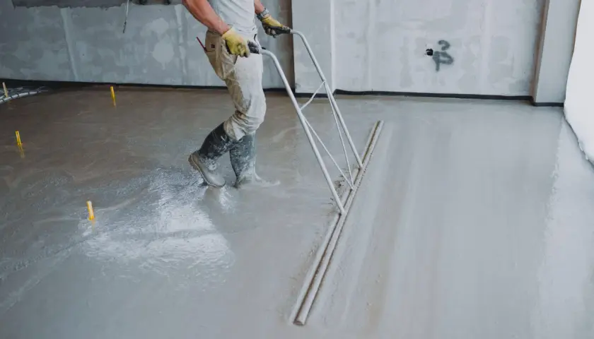 Robotnik wylewa beton na podłogę za pomocą zgarniacza.