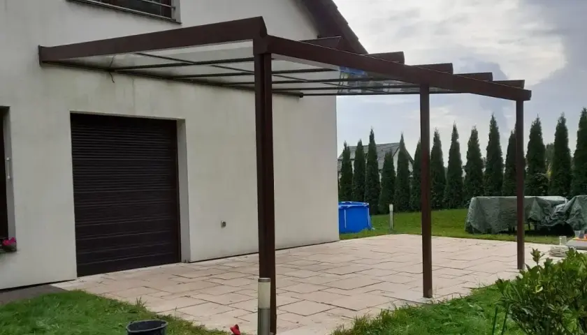 Nowoczesne zadaszenie tarasu z przezroczystym dachem, przyścienne, z brązową konstrukcją.