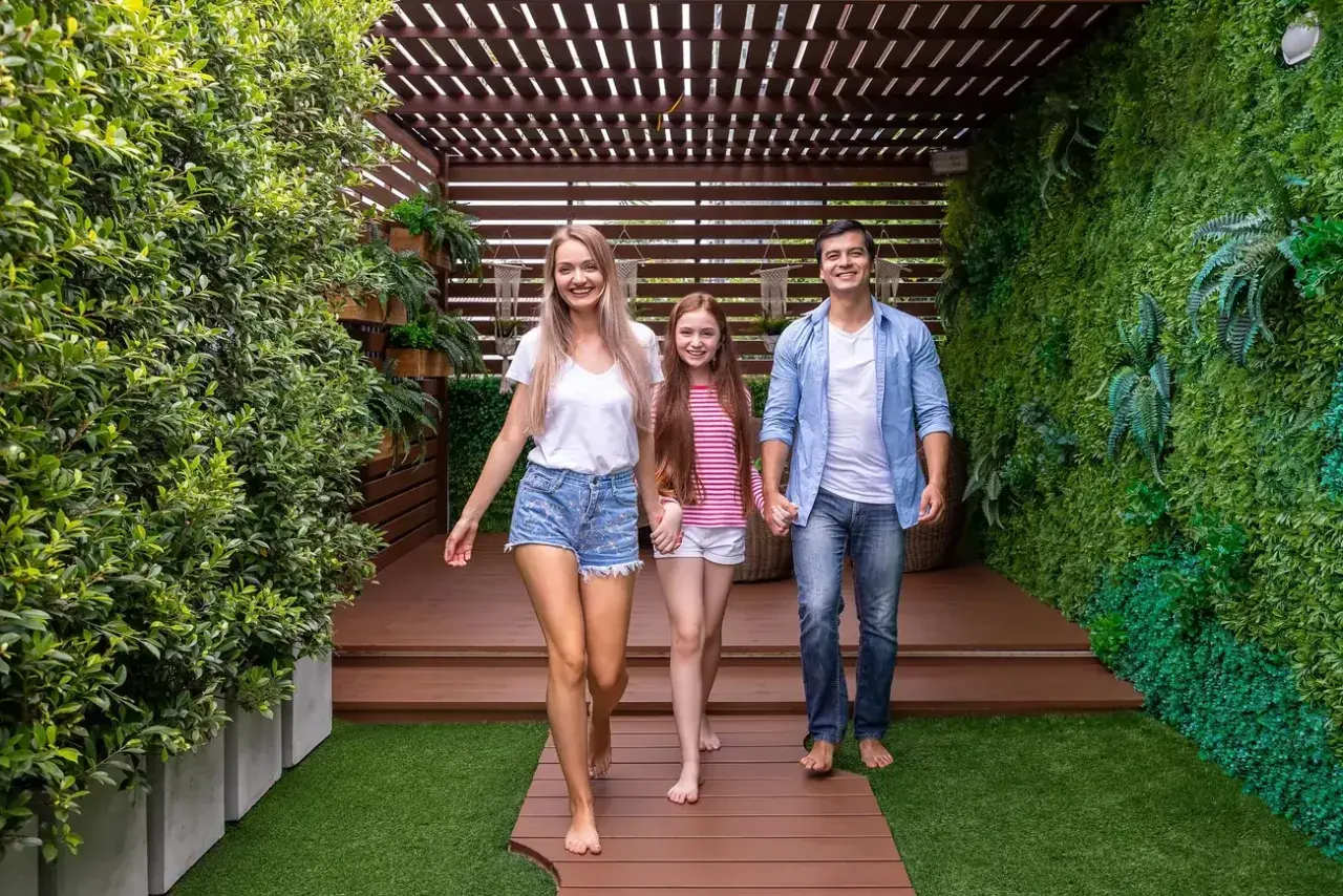 Rodzina idzie po drewnianej ścieżce na tarasie z zieloną ścianą i pergolą.